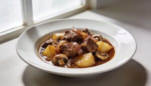 Close-up of a rich bowl of hearty caramelized onion beef stew with tender beef, potatoes, carrots, and mushrooms