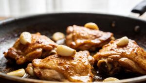 Close-up shot of a golden-brown, braised 40-clove garlic chicken with roasted garlic cloves, fresh herbs, and a rich white wine sauce in a cast iron skillet.