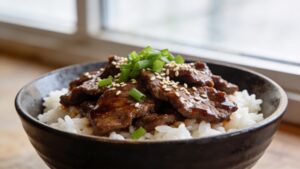 A vibrant quick teriyaki beef rice bowl with thin-sliced glazed beef, jasmine rice, sesame seeds, pickled cucumber, and green onions.