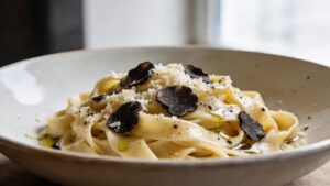 Silky tagliatelle pasta tossed with black truffle oil, parmesan, and black pepper in a white bowl