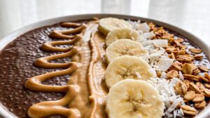 Chocolate chia pudding parfait layered with banana, almond butter, and coconut flakes in a clear glass