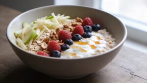 A beautiful glass bowl of Bircher muesli topped with fresh berries, sliced banana, toasted nuts, and a drizzle of honey