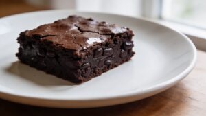 A square of fudgy black bean brownies on a white plate, drizzled with chocolate sauce and topped with raspberries