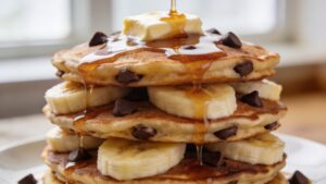 Golden banana chocolate chip pancakes with butter and maple syrup on a plate