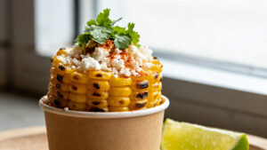 A cup of grilled corn elote with cotija cheese, chili powder, and lime