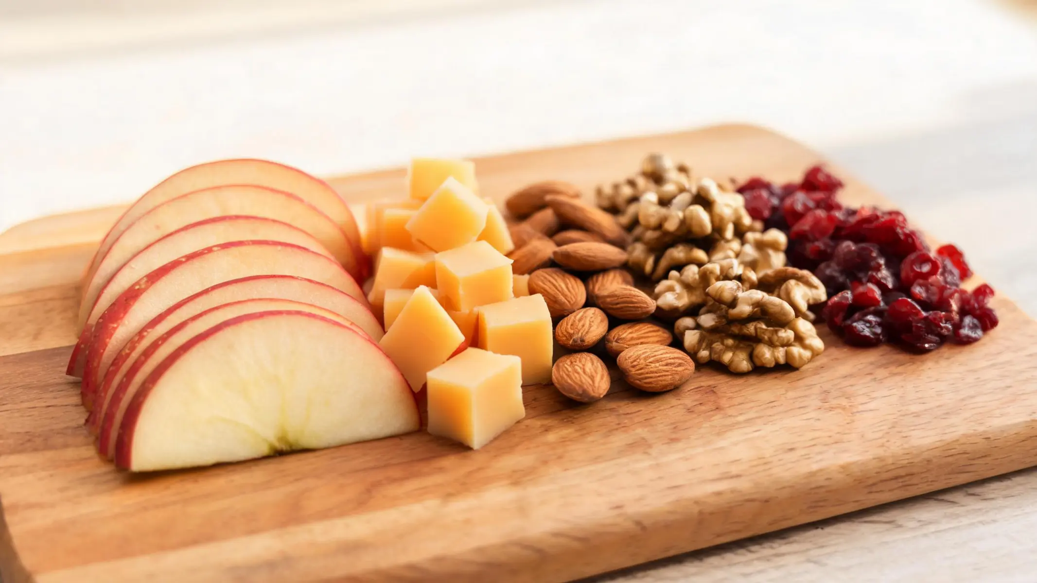 A wooden board filled with apple slices, cheddar cubes, nuts, and dried cranberries ready for snacking