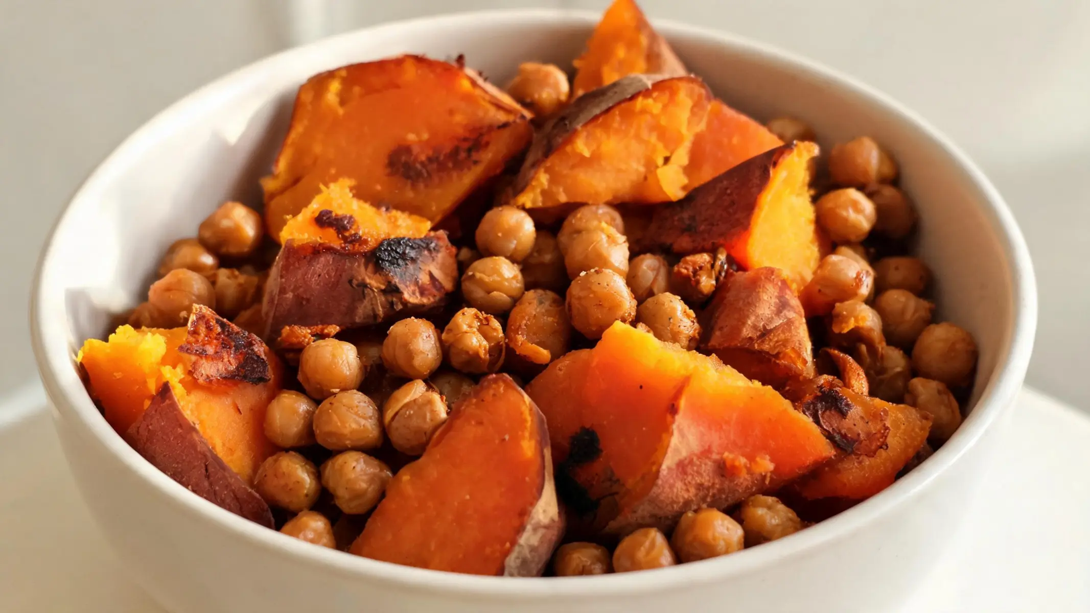 A hearty bowl of roasted sweet potatoes and chickpeas with fresh greens and dressing.