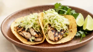 Plated grilled fish tacos with lime cabbage slaw on a wooden board