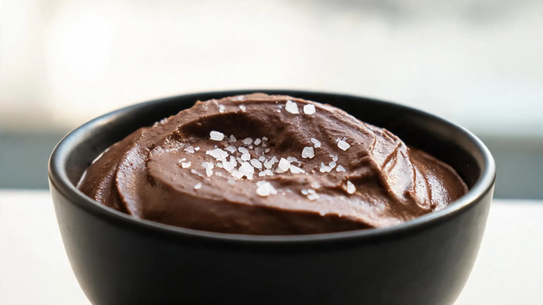Smooth keto chocolate avocado mousse in a glass with sea salt flakes on top