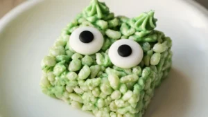 Green monster-face Rice Krispy treats with candy eyes on a plate