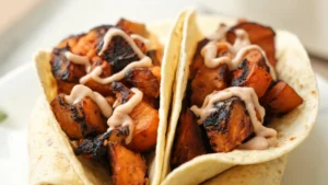 Plated roasted sweet potato tacos drizzled with chipotle crema, garnished with fresh cilantro and lime wedges
