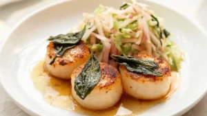 Plated sage brown butter scallops with apple slaw, garnished with fresh sage leaves