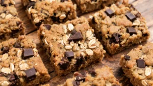 Stacked vegan candy cookie bars with melted chocolate and oats on a plate
