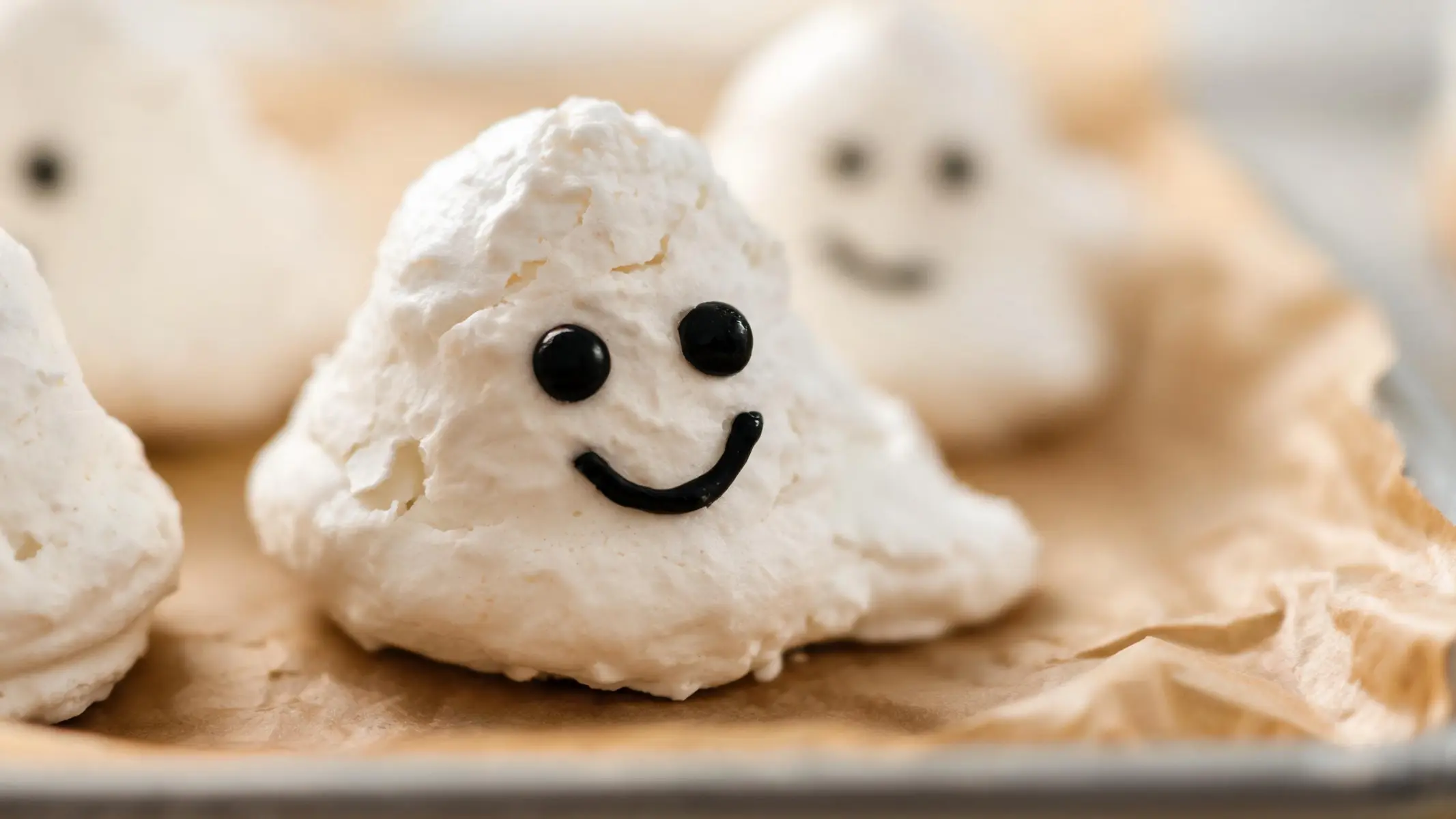 Platter of vegan ghost meringue cookies shaped like ghosts, dusted with powdered sugar