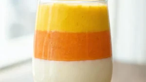 Vegan candy corn layered smoothie in a glass with mango, orange, and coconut cream layers