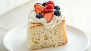 Angel food cake topped with fresh berries and yogurt cream on a serving plate