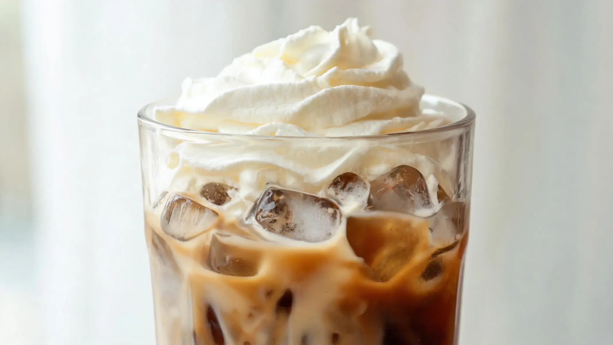 A tall glass of iced vanilla coffee frappe topped with whipped cream and a straw
