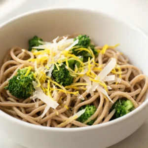 A bowl of lemon broccoli whole-wheat pasta garnished with lemon slices and fresh herbs