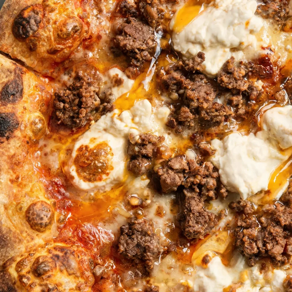 Hot honey sausage pizza with creamy ricotta, topped with fresh basil and red pepper flakes on a wooden board