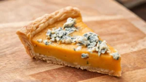 A golden-brown roasted pumpkin and blue cheese tart on a wooden board, garnished with fresh herbs.