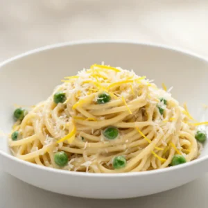 A bowl of creamy lemon parmesan pasta with peas, garnished with lemon zest and parmesan cheese.