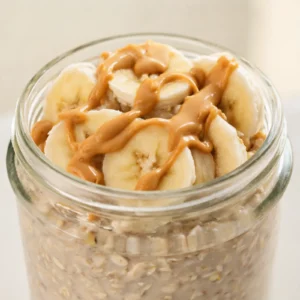 A jar of creamy peanut butter banana overnight oats topped with sliced bananas and a drizzle of peanut butter